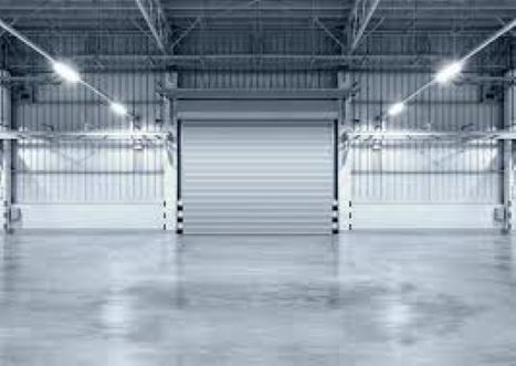A large warehouse with a door open and lights on.